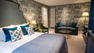 Une chambre avec un grand lit, un fauteuil vert, un canapé gris et une petite table ronde.