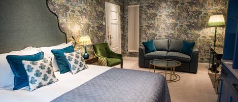 A bedroom with a large bed, a green armchair, a grey sofa, and a small round table.
