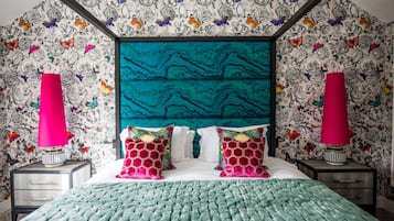 Un dormitorio con cabecera color aguamarina, papel tapiz estampado y lámparas rosadas.