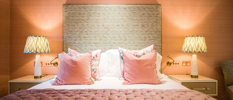 A neatly made bed with a pink quilt, two bedside lamps, and a headboard with a textured design.