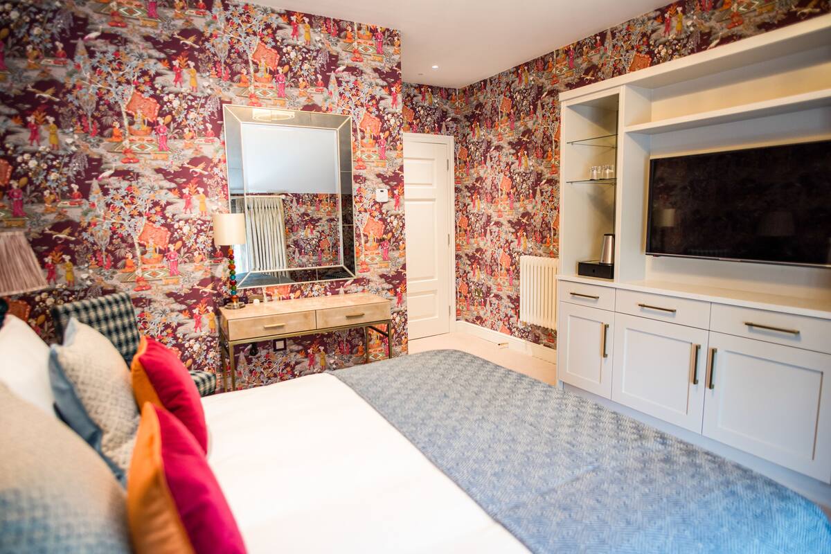 A bedroom with a large bed, a dresser, a TV, and a mirror.
