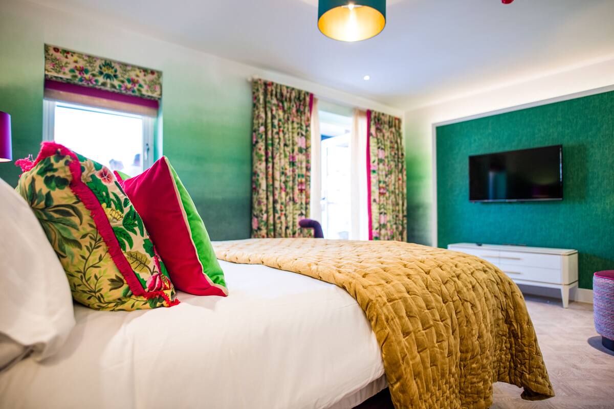 A bedroom with a large bed, a flat-screen TV, and a window with curtains.