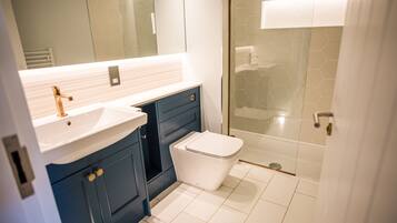 Une salle de bain moderne avec un lavabo blanc, des meubles bleus et une douche à l’italienne en verre.