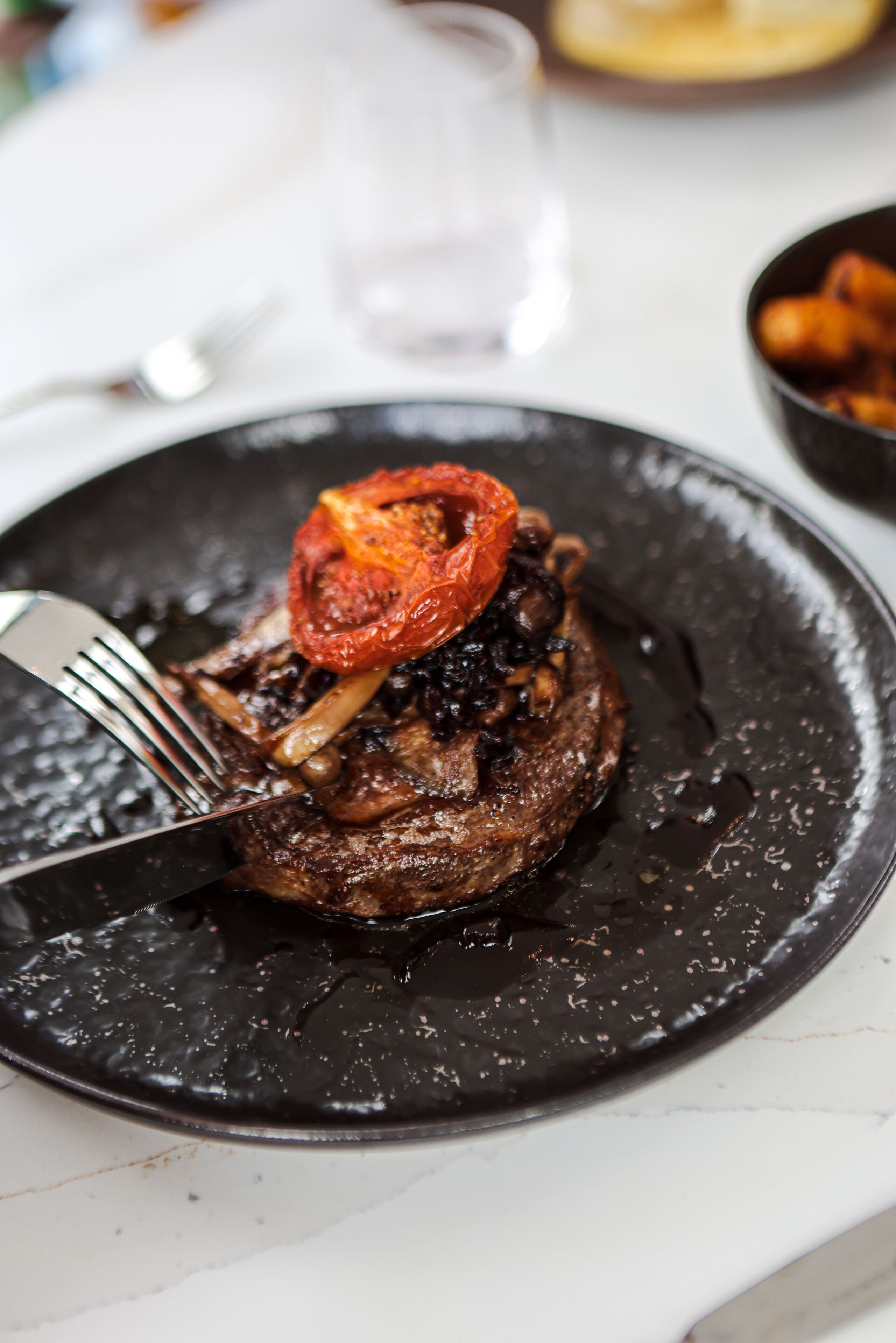A plate with a steak topped with mushrooms and a slice of tomato.