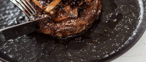 A plate with a steak topped with mushrooms and a slice of tomato.