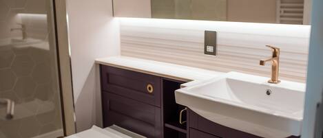 Un baño moderno con inodoro blanco, muebles oscuros y lavamanos blanco con grifo dorado.