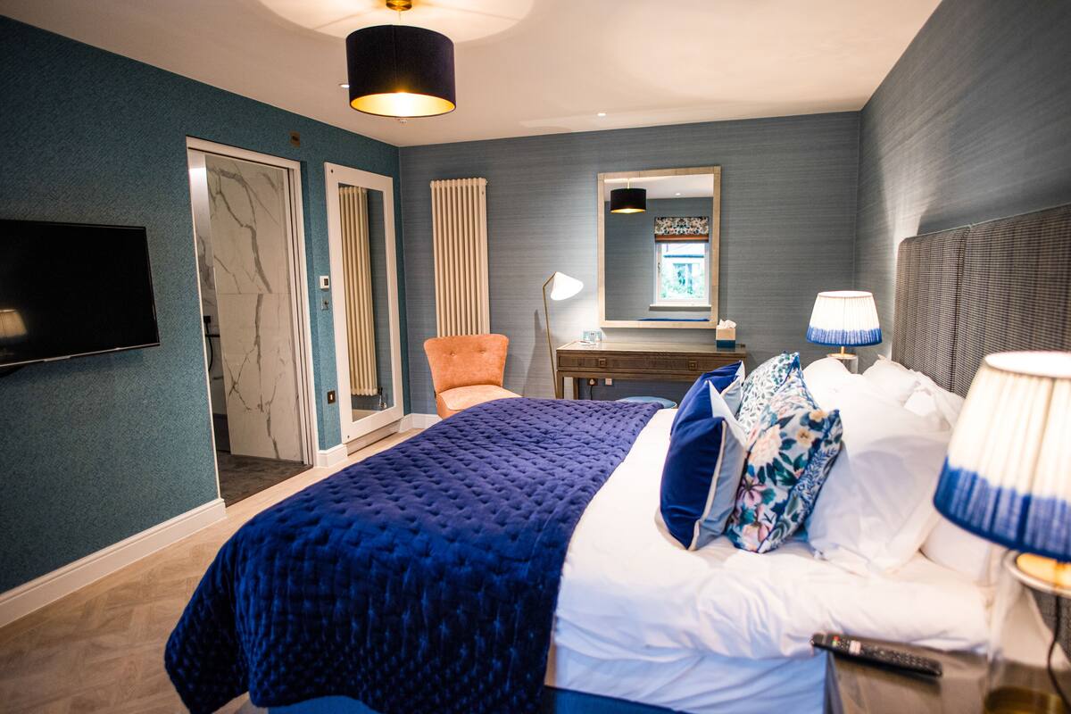A bedroom with a large bed, a TV, a mirror, and a nightstand.