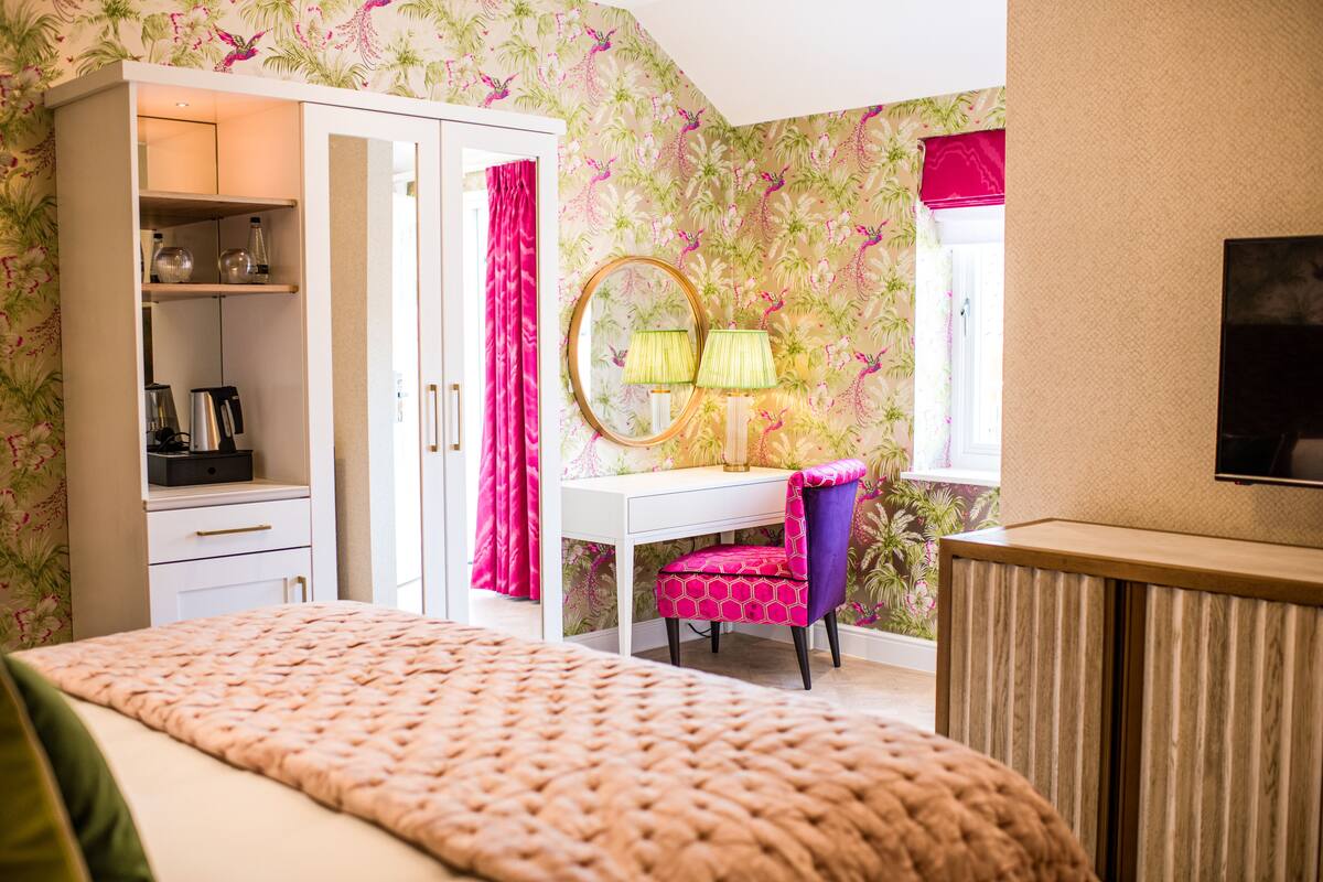 A bedroom with a bed, a wardrobe, a desk with a chair, a mirror, and a television.
