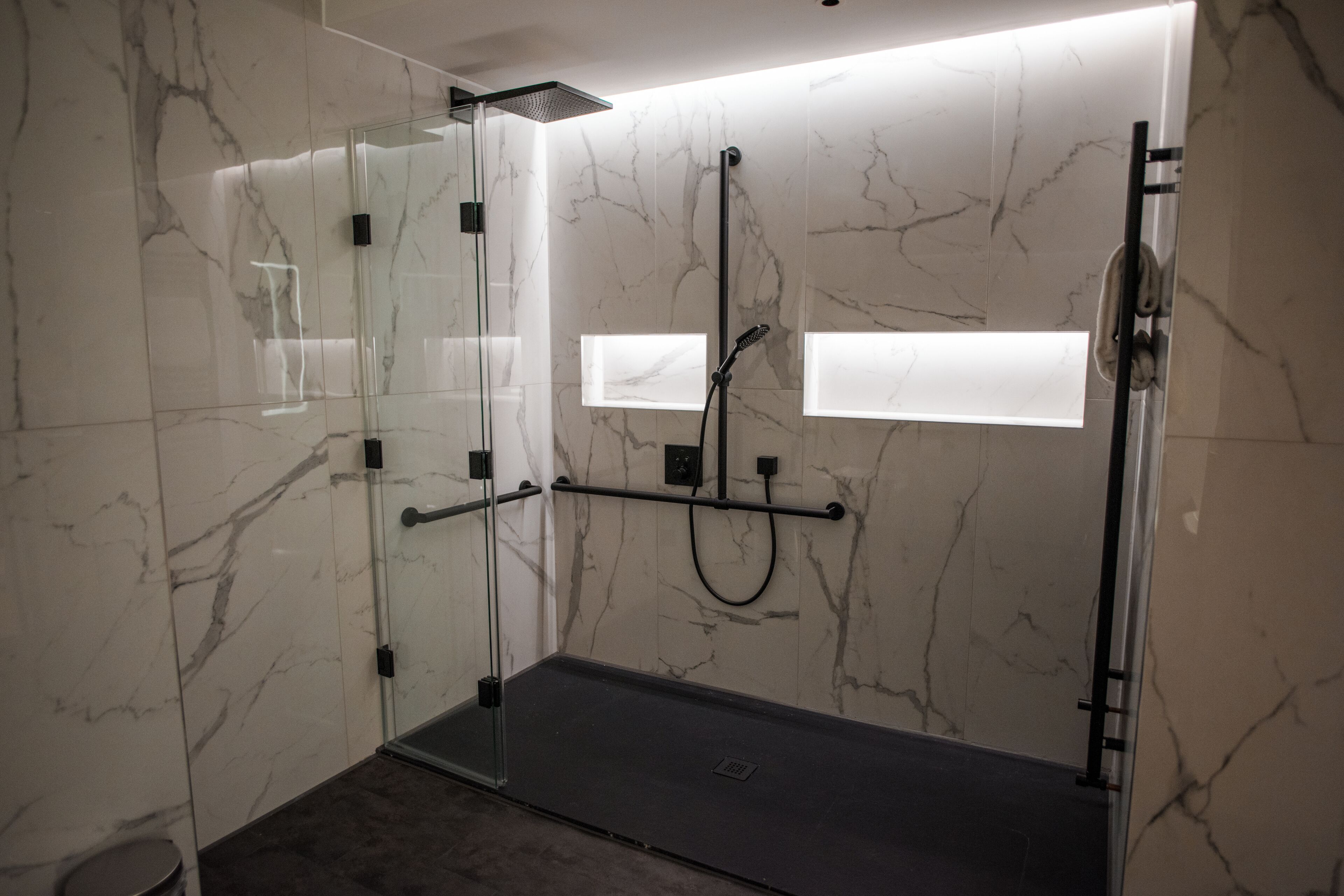 A modern shower area with glass doors, a handheld showerhead, and a control panel.