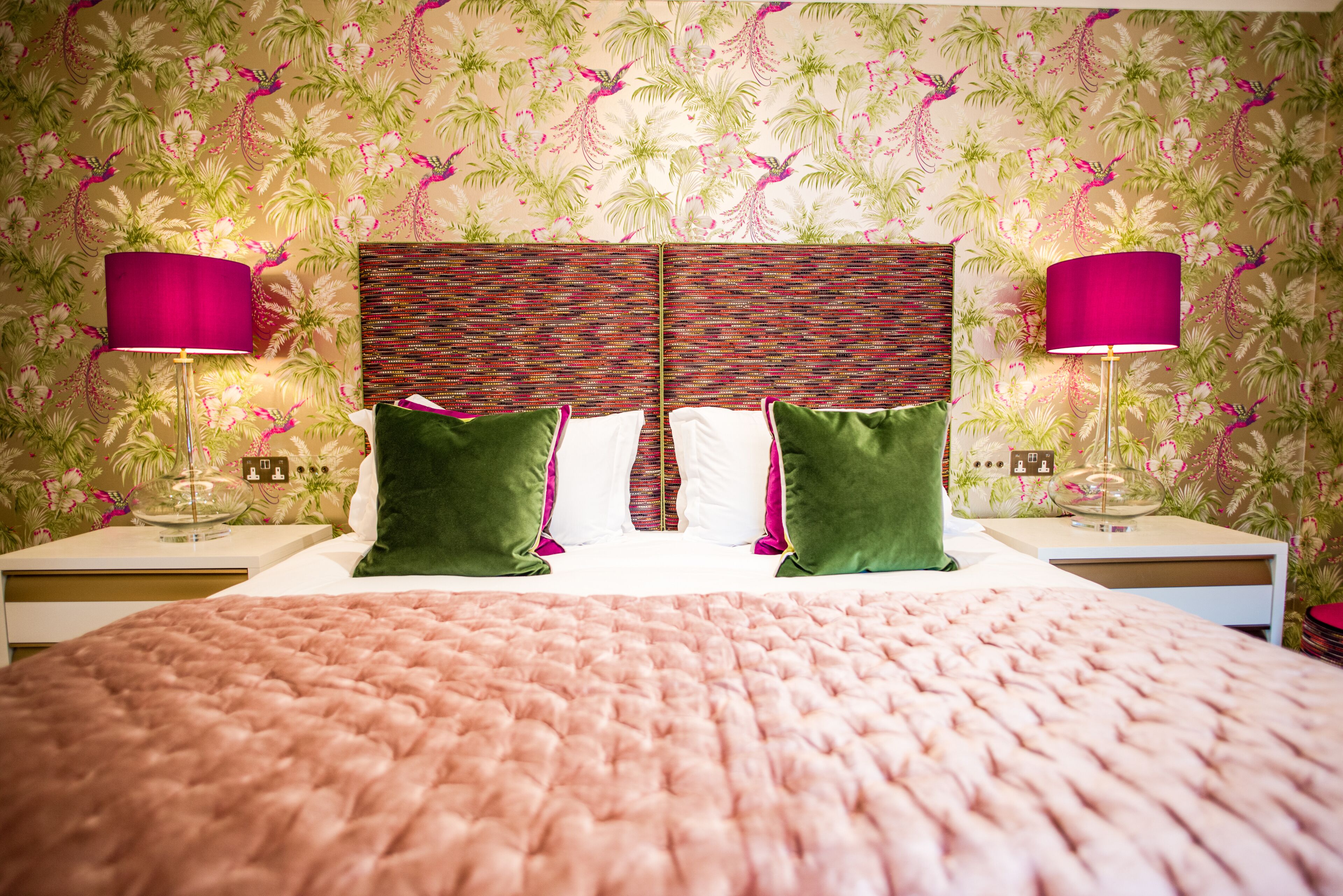 A bedroom with a large bed, two nightstands, two lamps, and a floral wallpaper.