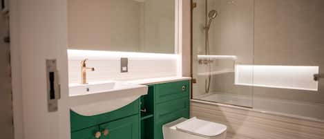 A modern bathroom with a white sink, green cabinets, a white toilet, and a glass-enclosed shower area.