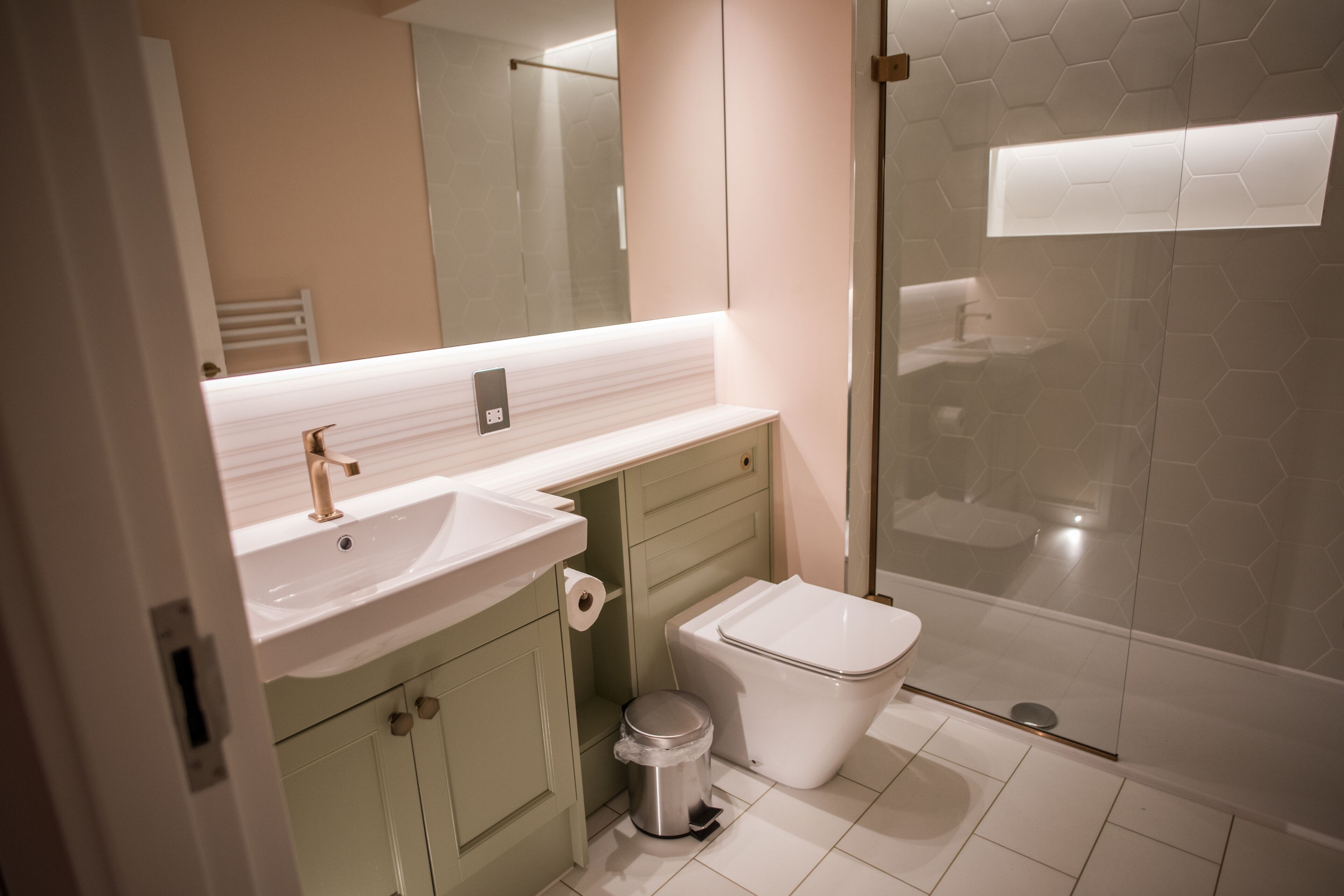 A modern bathroom with a white sink, green cabinets, a toilet, and a glass shower enclosure.