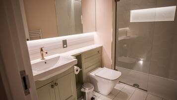 A modern bathroom with a white sink, green cabinets, a toilet, and a glass shower enclosure.