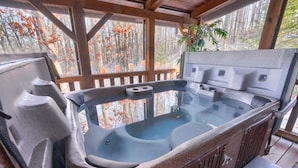 A hot tub with a wooden deck and a view of autumn trees.