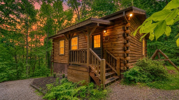 A wooden cabin with a porch, windows, and a staircase leading to the entrance.
