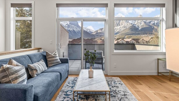 Een moderne woonkamer met een bank, salontafel en uitzicht op bergen door grote ramen.