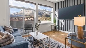 Een moderne woonkamer met een groot raam, een flatscreen televisie, een bank, een salontafel en een lamp.