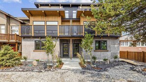 Een modern huis met twee verdiepingen, een gevel van natuursteen, een balkon en een kleine tuin met jonge bomen en rotsen.