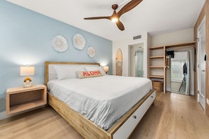 Une chambre à coucher comprenant un lit, des tables de chevet, un ventilateur de plafond et un dressing.