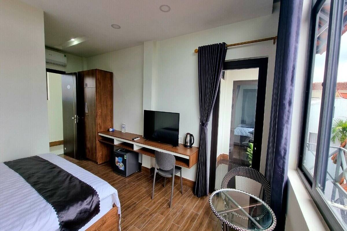A hotel room with a bed, a desk with a TV, a small fridge, and a window with curtains.