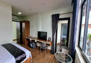 A hotel room with a bed, a desk with a TV, a small fridge, and a window with curtains.