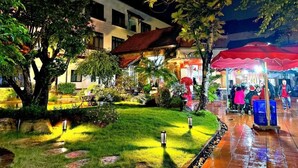 Un patio luminoso con un pequeño jardín, una sombrilla roja y un edificio con varias ventanas.