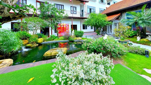 Un patio con un estanque, abundante vegetación y un edificio con varios balcones.
