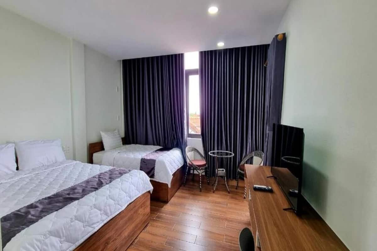 A hotel room with two beds, a small table, chairs, a TV, and a window with curtains.