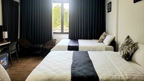 Habitación de hotel con dos camas, un escritorio, una silla y un ventanal con cortinas.