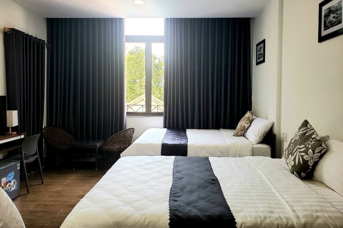 A hotel room with two beds, a desk, a chair, and a window with curtains.