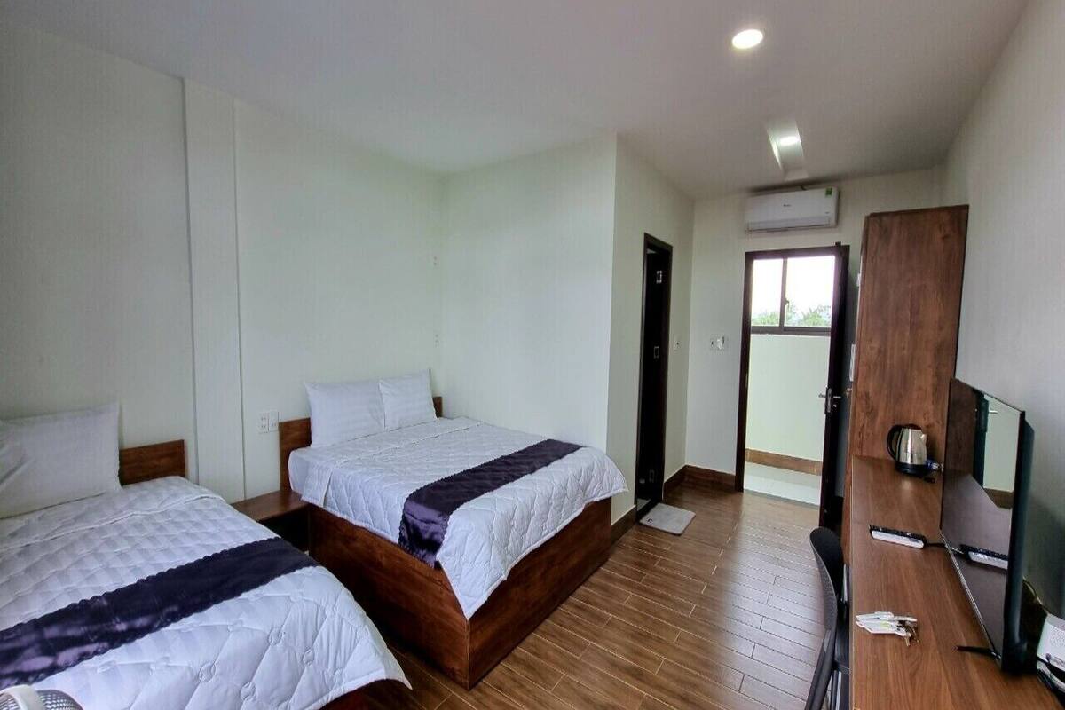 A hotel room with two beds, a desk, a TV, and an air conditioning unit.