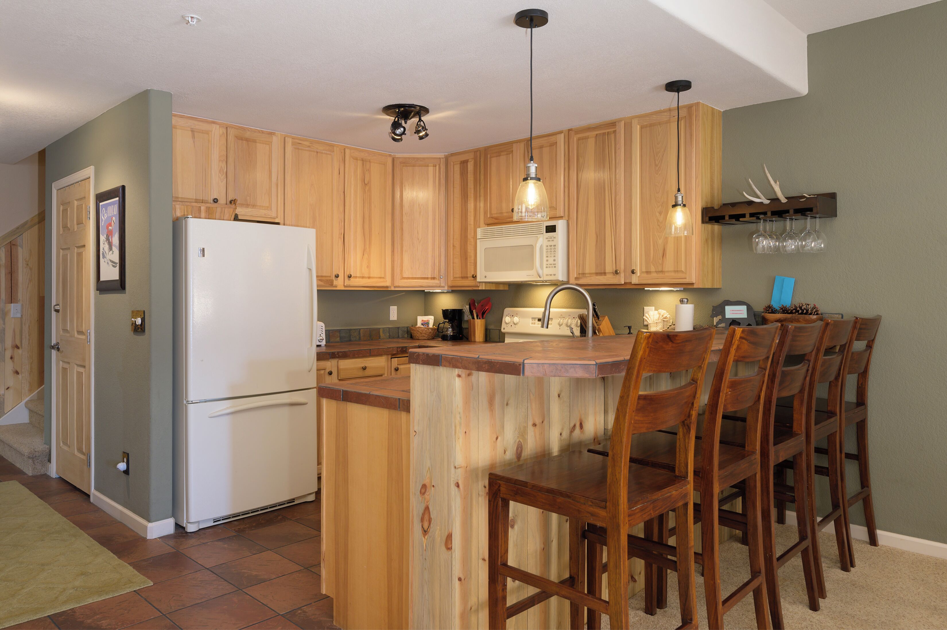 A kitchen with wooden cabinets, a white refrigerator, a microwave, a sink, and a bar area with chairs.