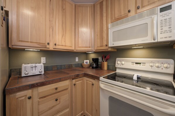Una cocina con armarios de madera, un microondas blanco, una estufa y un tostador.