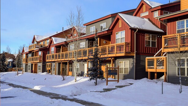A row of multi-story wooden buildings with balconies, a covered walkway, and a snow-covered ground. - Waterside West E206 Fraser 2 bedroom open floor plan & lots of amenities (Fraser)