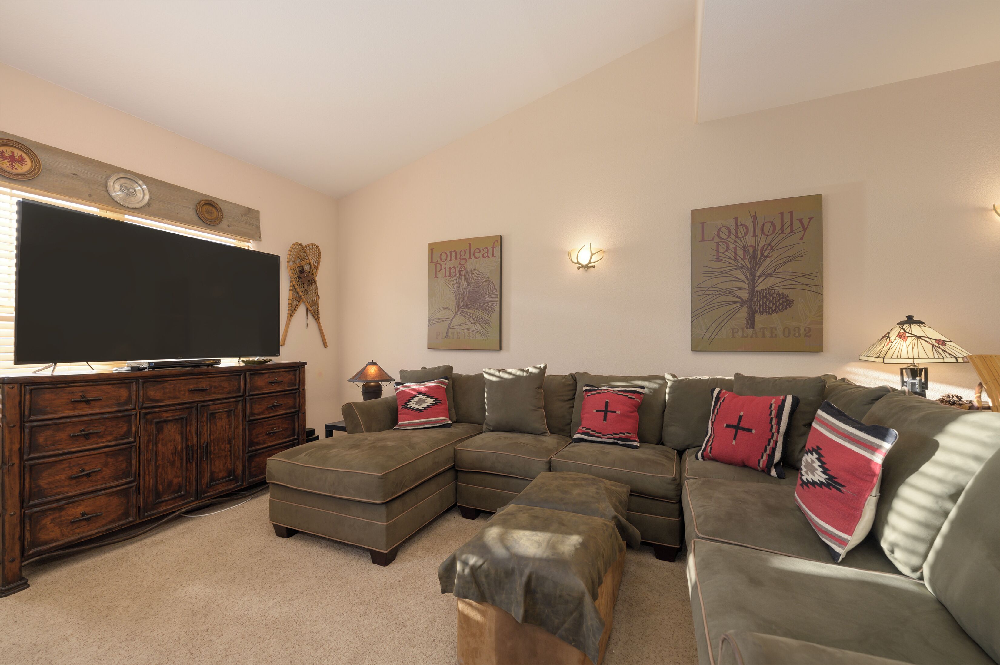 A living room with a sectional sofa, a flat-screen TV, a wooden cabinet, and wall-mounted artwork.