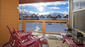 A wooden deck with red chairs and benches, overlooking a snowy landscape with houses and a clear sky. - Waterside West E206 Fraser 2 bedroom open floor plan & lots of amenities (Fraser)