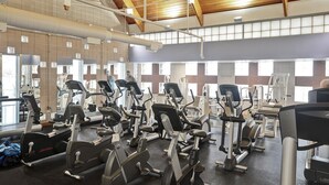 Ett gym med flera träningsmaskiner, ett högt tak med synliga träbjälkar och stora fönster som släpper in naturligt ljus.