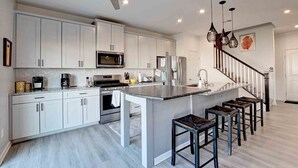 A modern kitchen with white cabinets, a central island, and bar stools.