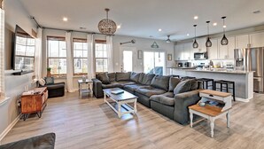 A modern living room with a sectional sofa, a wooden coffee table, and a kitchen area with stainless steel appliances.