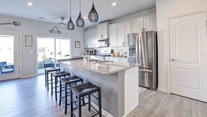 A modern kitchen with white cabinets, a stainless steel refrigerator, and a central island with bar stools.