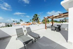 A rooftop terrace with two sun loungers, a table with chairs, and a pergola.