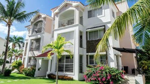 A multi-story building with balconies, a covered patio, and a well-maintained garden with palm trees and flowering plants.