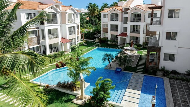 A residential complex with a swimming pool surrounded by greenery and palm trees.