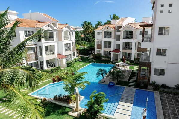A residential complex with a swimming pool surrounded by greenery and palm trees.