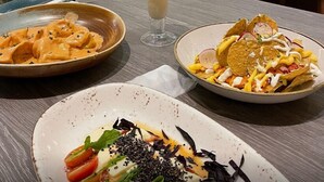 A restaurant interior with a table set for a meal, including a creamy drink, pasta, a taco salad, and a fresh salad with cheese and greens.