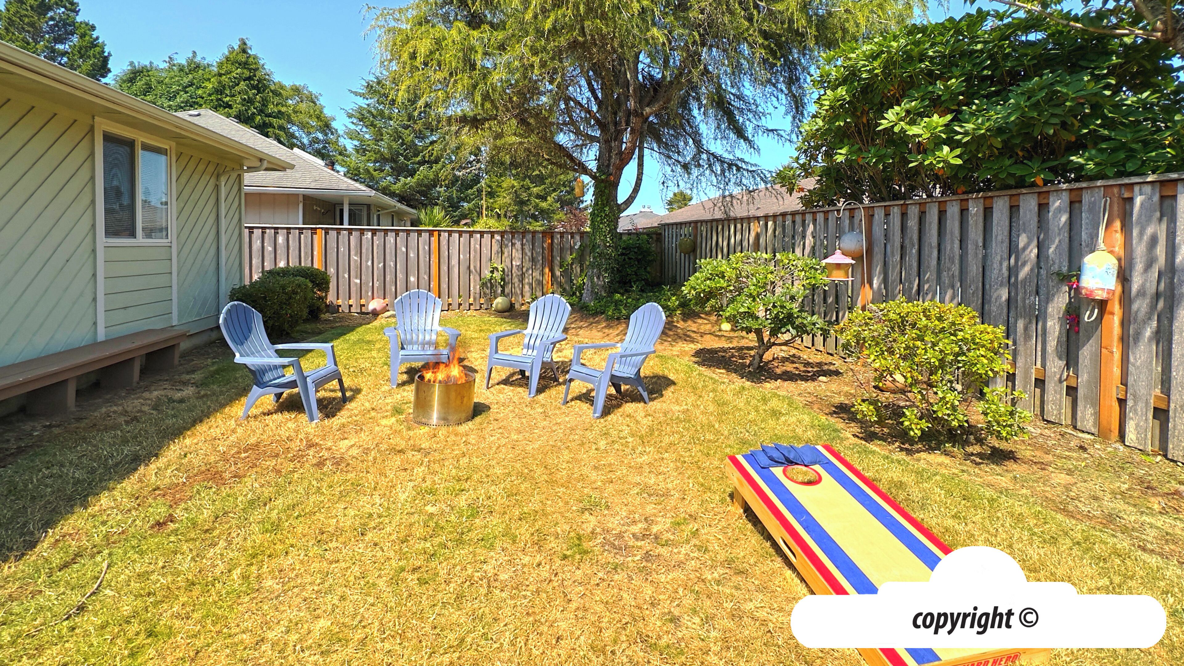 Ein Garten mit Feuerstelle, vier Adirondack-Stühlen, einem kleinen Tisch und einem bunten Spielbrett.