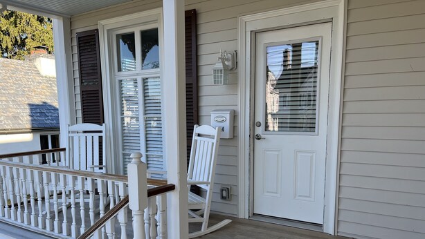 Une véranda en bois avec une balustrade blanche et une chaise berçante blanche.