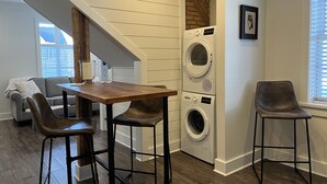 Un espace de vie compact comprenant un coin repas, deux tabourets de bar, un lave-linge et un escalier.