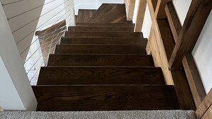 Un escalier en bois, avec un mur blanc et une main courante en bois.