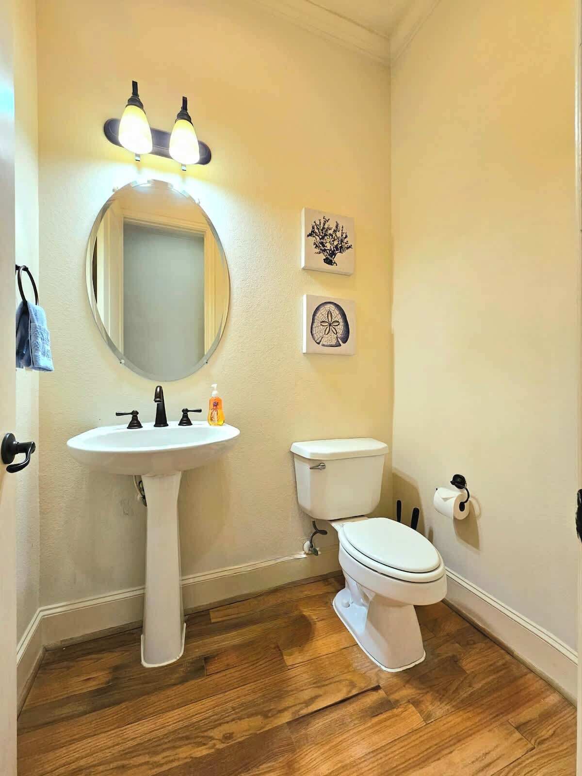 Une salle de bain avec un miroir rond, un lavabo blanc, des toilettes et deux appliques murales.